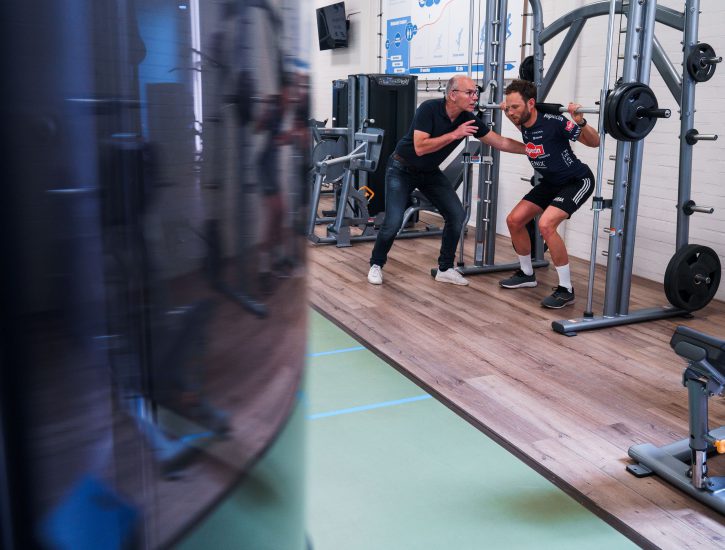 Patient voert een squat uit onder begeleiding van een fysiotherapeut in de oefenzaal van Gezondheidscentrum van der Toolen